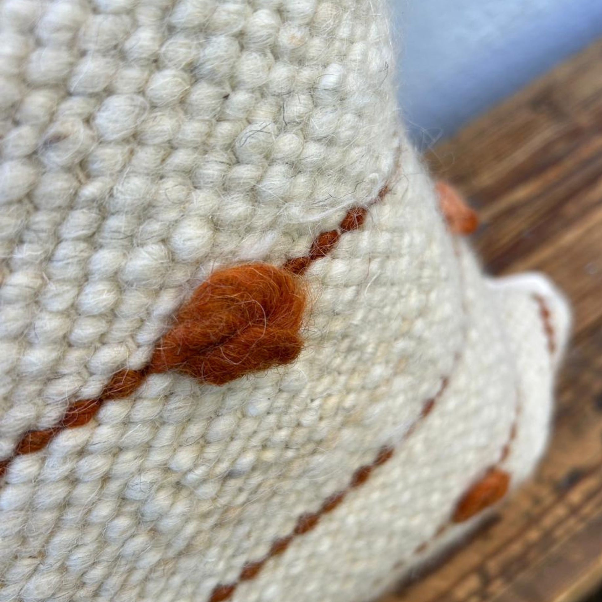 Close-up of a textured woven cushion cover with orange accents on a wooden surface