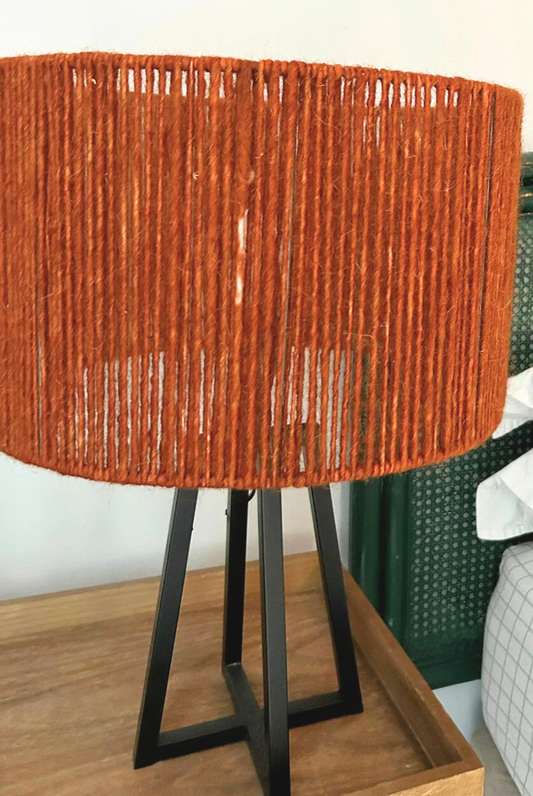 Table lamp with a orange woven shade on a wooden surface